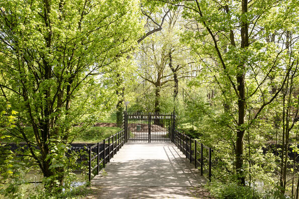 toegangsbrug richting toegangshek met bomen aan de zijkant