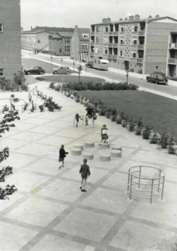 vergroot de afbeelding; tussen de flats ligt een open strook met rechthoekige vormen in de bestrating, met een paar speeltoestellen daarin. Het grootste deel is open vlakte, met aan de ene kant een rechte rij paaltjes, en aan de andere kant een rechte rij boompjes.