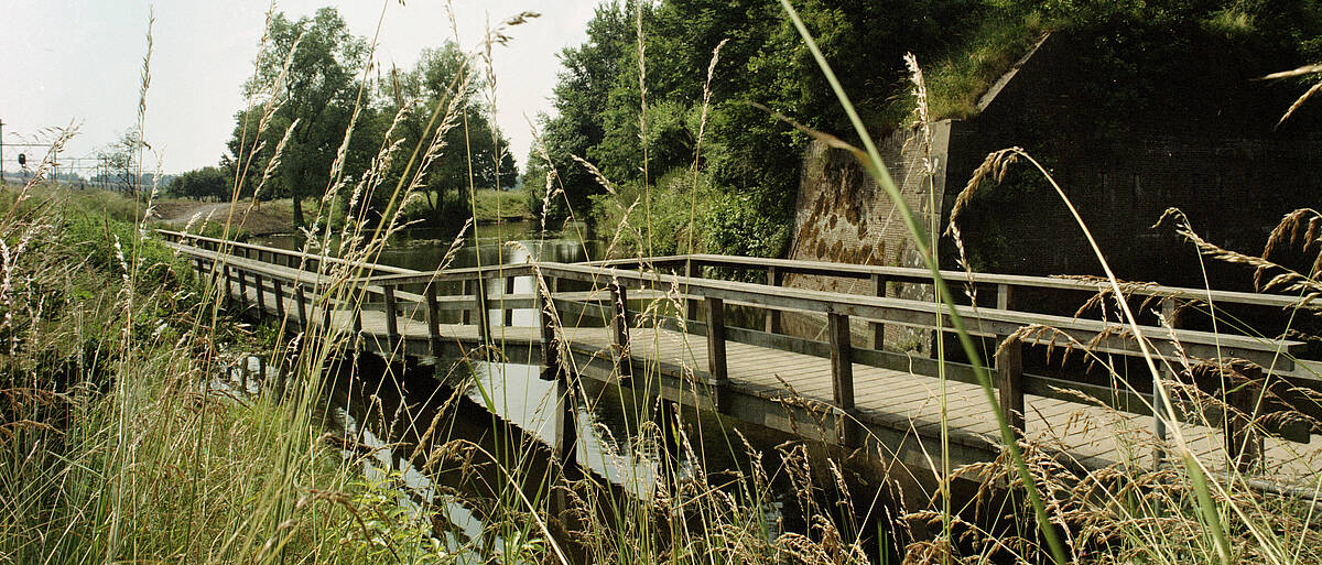 Gezicht op de fiets- en voetgangersbrug in het Ravelijnpad in het Beatrixpark te Utrecht; rechts het Lunet 3. (Collectie Het Utrechts Archief)